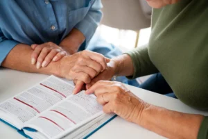 Idosas de mãos dadas leem e apontam para trecho de livro aberto, em momento de apoio e conversa sobre herança.