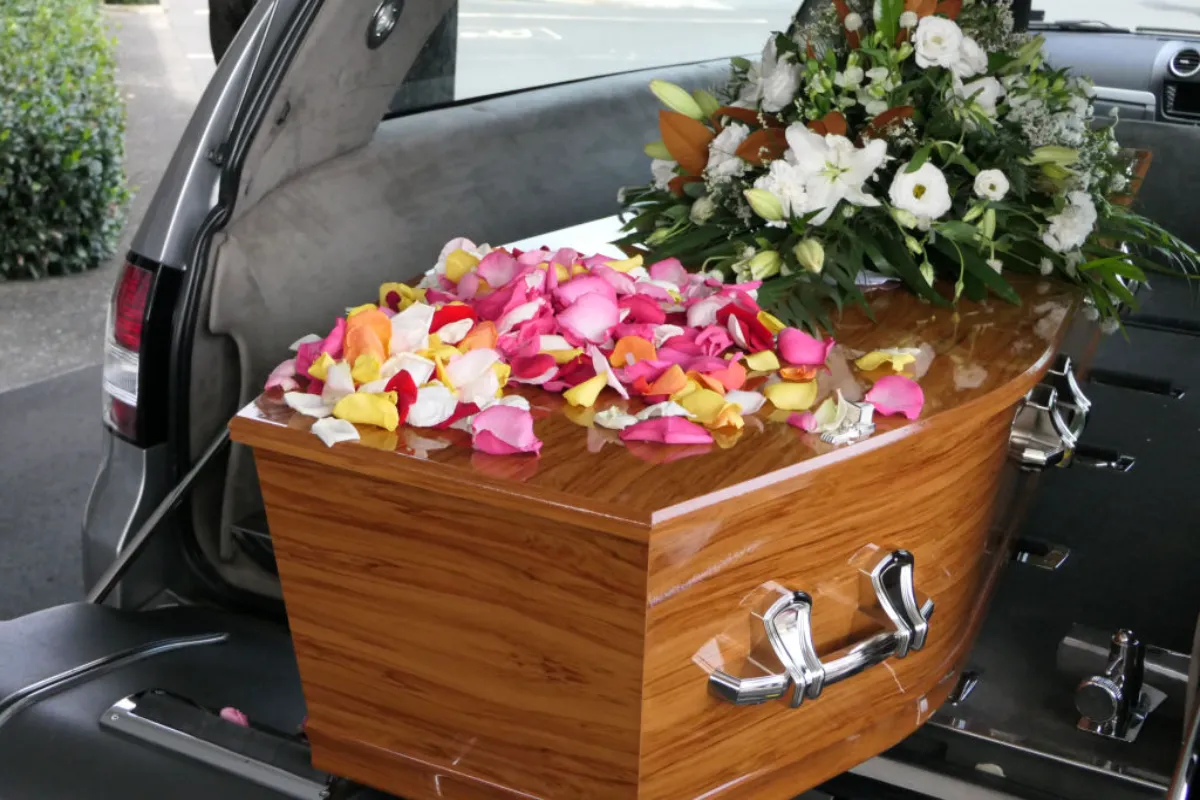 Caixão com flores sendo transportado em carro funerário.