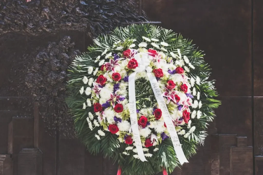 Ornamentação de velório com coroa de flores brancas, rosas vermelhas e folhagens em ambiente funeral.