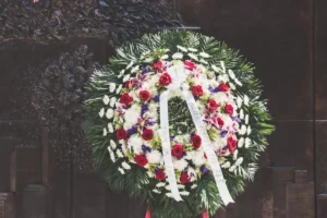 Ornamentação de velório com coroa de flores brancas, rosas vermelhas e folhagens em ambiente funeral.