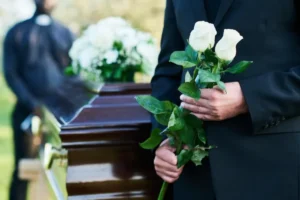 Velório com caixão, flores brancas e pessoa de luto, tema relacionado a quanto custa um velório e enterro