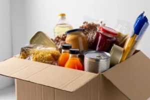 Seguro cesta básica com caixa de alimentos não perecíveis, massas, enlatados, sucos e outros itens.